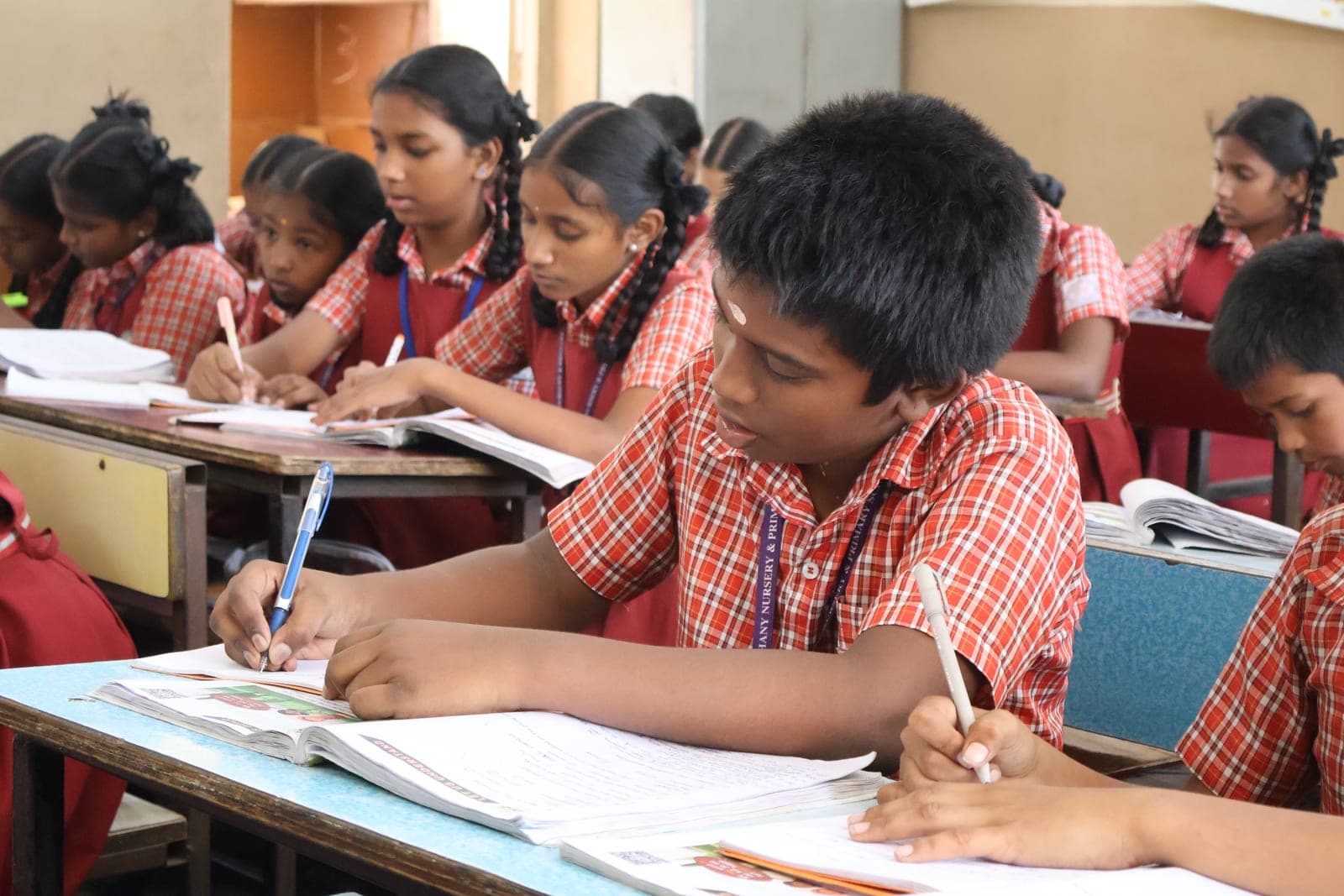 CMCT ஆதரவு பெறும் வகுப்பறையில் தங்கள் மேசைகளில் எழுதும் சிறுவர்கள்